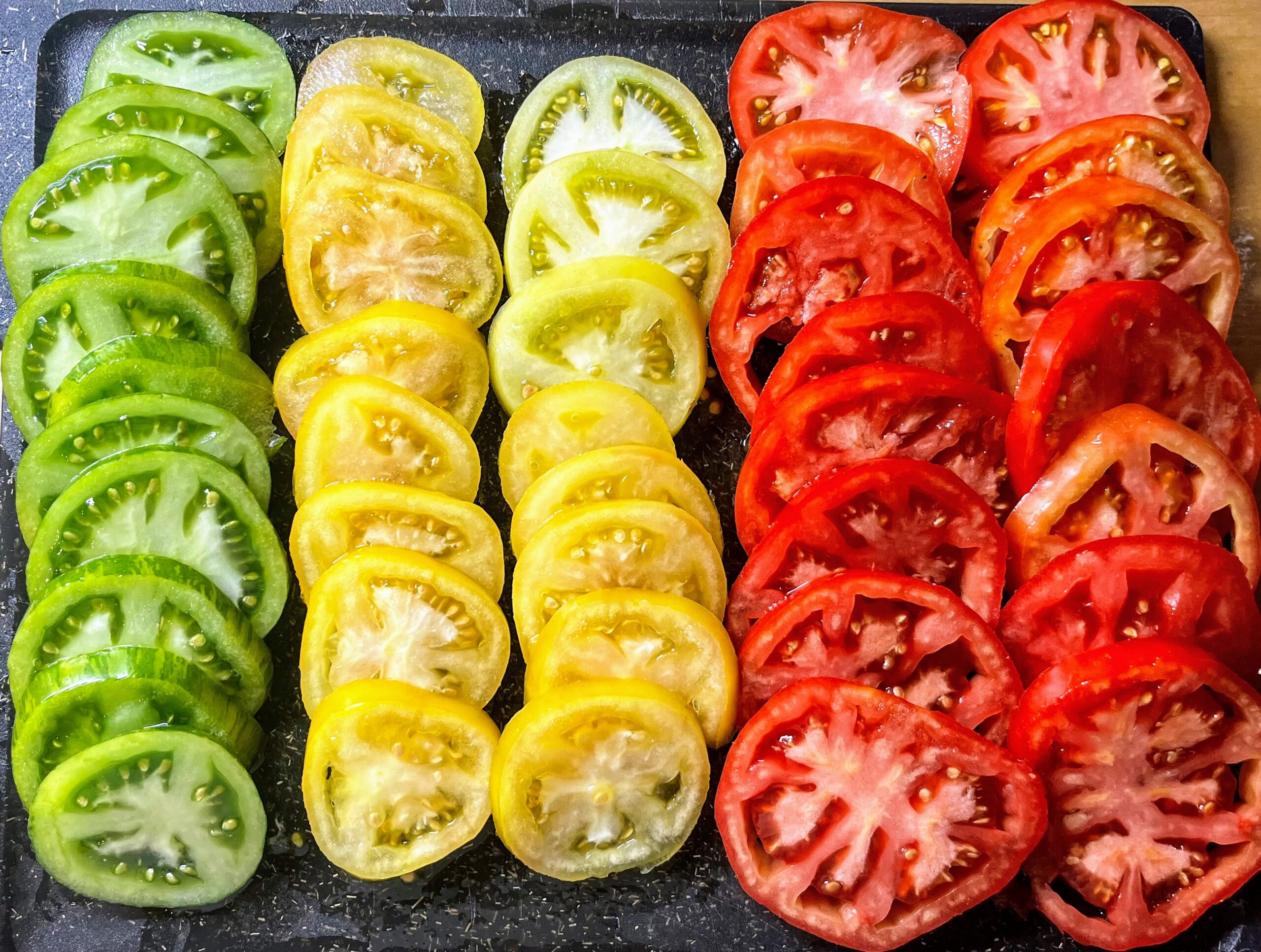 Tomates vertes, jaunes et rouges coupées en tranches et placées sur une planche en rangées.